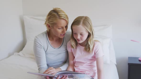 Front view of Caucasian woman reading a story to her daughter on bed