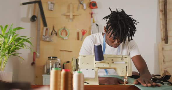 Focused african american craftsman with dreadlocks using sewing machine in leather workshop