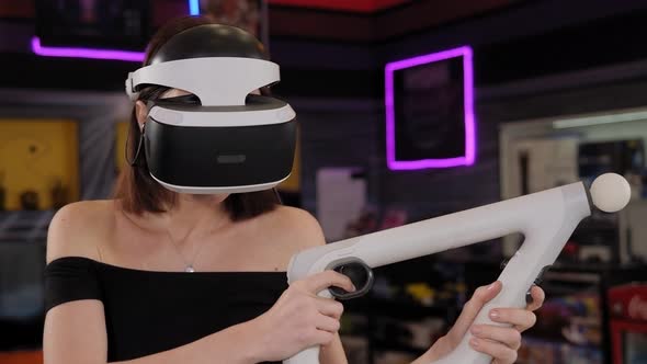 Woman Playing Game Using Virtual Reality Headset and Gamepads in Playing Club