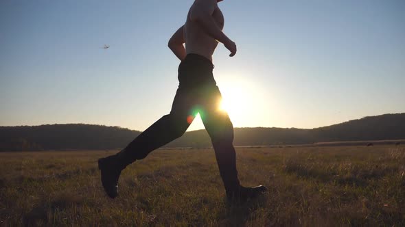 Young Muscular Man Running Through Field with Beautiful Landscape at Background