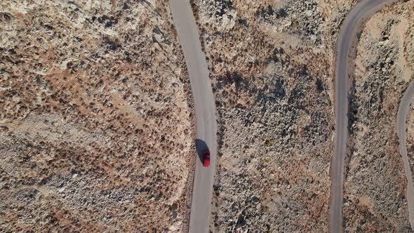 Drone shot of small car driving along the narrow curve road above rocks