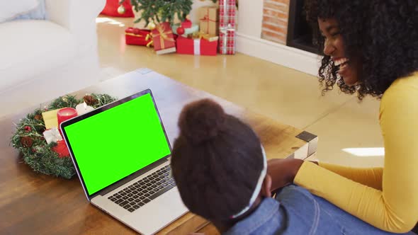 African american mother and daughter using laptop with green screen at home