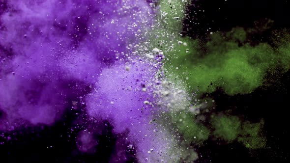 Colorful powder/particles fly after being exploded against black background. Slow Motion.