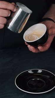 Barista pouring milk in hot coffee and making cappuccino foam in cafe close up, vertical