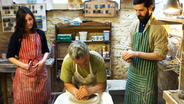 Colleagues looking at potter while making a earthen pot on a pottery wheel