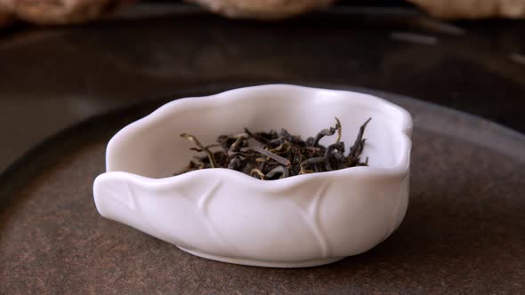 Dry Green Tea Poured Into White Bowl Close Up. Chinese Tea Falling in Porcelain Bowl for Traditional