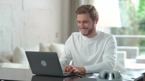 Cheerful Caucasian Man Sits at Home on the Desk and Works Using a Laptop Financial Manager on a