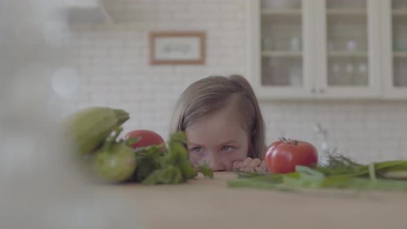 Small Girl Looking at the Table with Tomatoes Zucchini Greens Onion