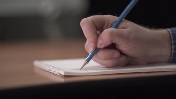 Man's Hand Writes with a Pencil on a Piece of Paper