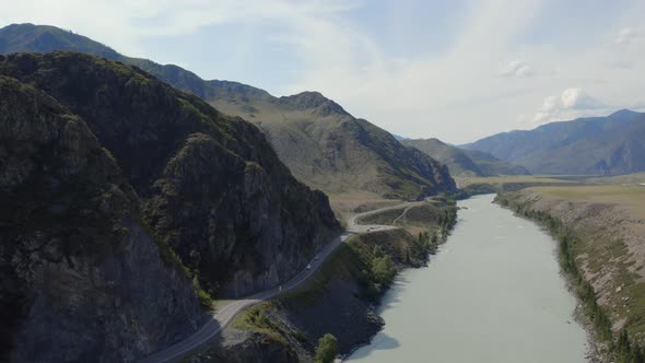 Traffic cars on Chuya highway road between mountains and Katun river under blue sky in Altai