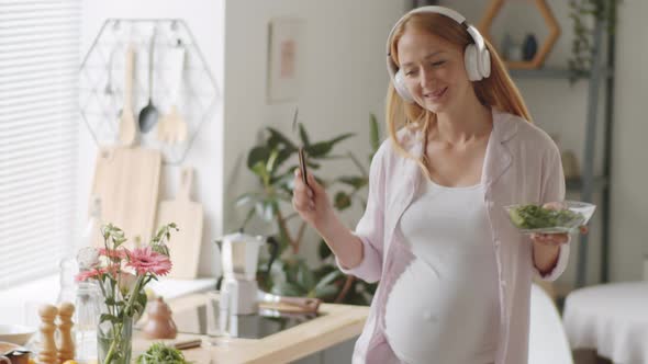Pregnant Woman in Headphones Dancing and Singing at Home