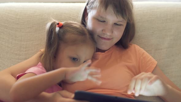 Two Girls Children Sister At Home On Couch Playing On Tablet