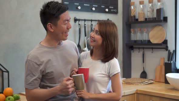 asian couple are drinking a cup of coffee together in the kitchen.
