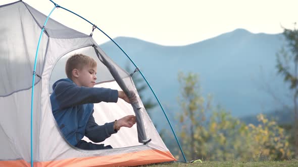 Hiker child boy sitting inside a tent in mountain campsite enjoying view of nature.