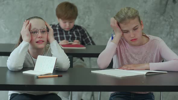 Bored Girl Sitting at Desk in School Classroom, Discussing Something with Classmate