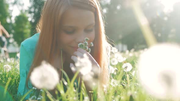 Beauty Girl lying on dandelions meadow and smelling flowers. Beautiful Spring Young Woman with red h