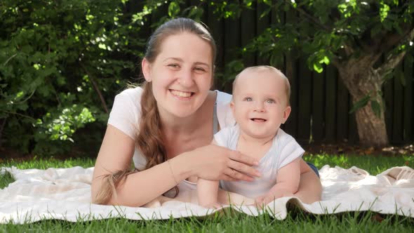 Cute Baby Boy and Mother Smiling in Camera While Lying on Green Grass in Garden or Park