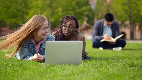 Diverse Friends Students Lying Outdoors on Lawn with Laptop Chatting and Smiling