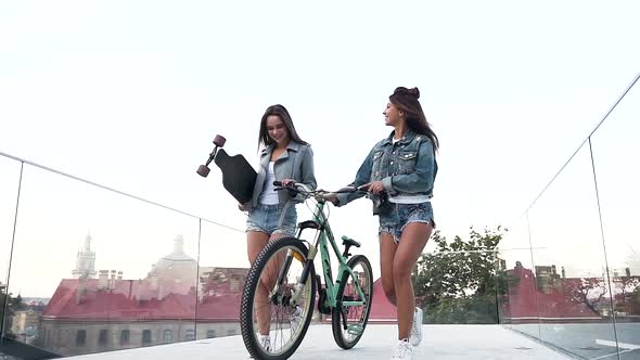 Young Ladies in Fashion Clothes Walking with Bicycle and Skateboard on the Glass Observation Deck