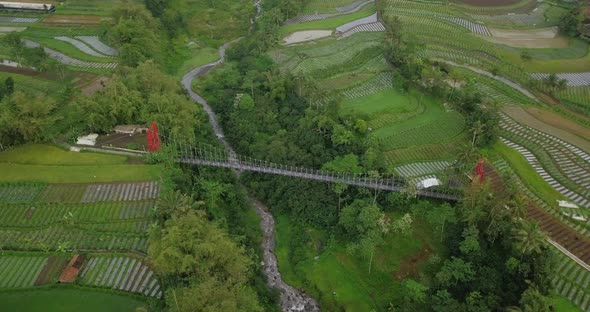 Rural drone shot of metal suspension bridge build over valley with river on the bottom and surrounde