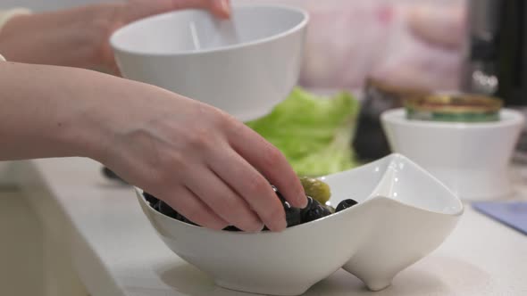 Woman Cooking Festive Dinner in the Kitchen Putting Olives in Serving Dish on Kitchen Counter