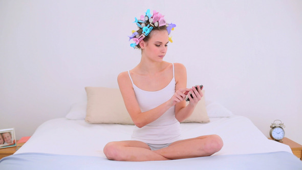 Young Model In Hair Rollers Sending A Text On Bed