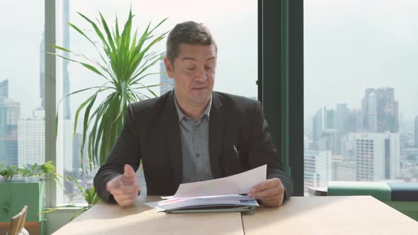 Businessman working through documents and shows paperwork statistics in online video conference