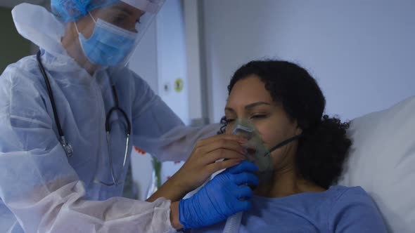 Caucasian female doctor putting on oxygen mask ventilator on african american female in hospital