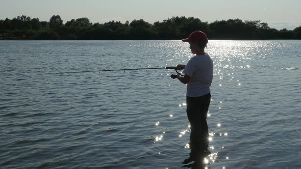 Silhouette of Little Boy Fishing on River at Sunset