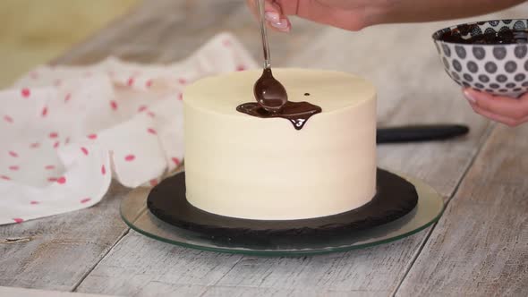 Closeup of a Pastry Chef Pouring Liquid Chocolate on a White Cream Cake