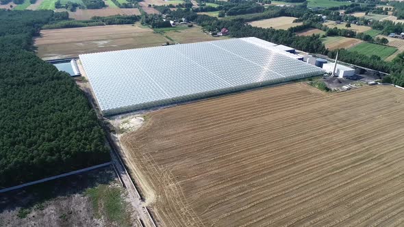 drone fly above a greenhouse with solar panel and sun shine reflection close to a plowed land field