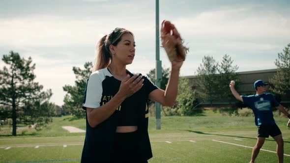 A female softball player warms up on a turf field for practice while she catches and throws the ball