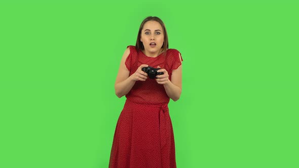 Tender Girl in Red Dress Is Playing a Video Game Using a Wireless Controller and Rejoicing in