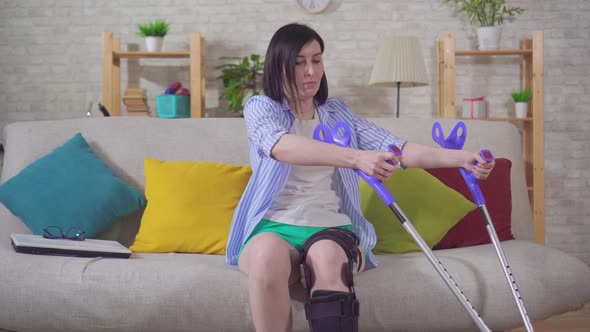 a Young Woman After Injury Knee Bend Orthosis Knee Brace Using Crutches Gets Up From the Sofa