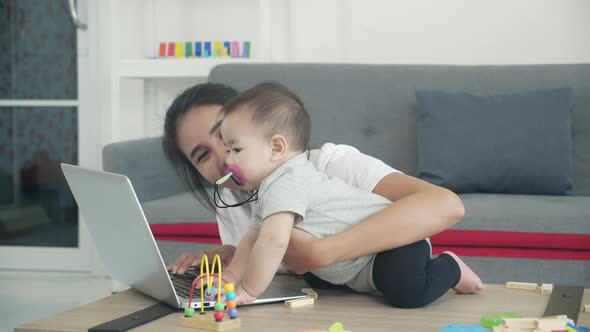 Happy young asian mom and baby girl using laptop computer for learning together in living room.