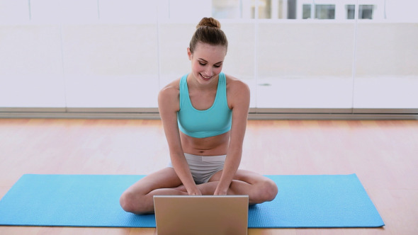 Fit Model Sitting On Exercise Mat Using Her Laptop