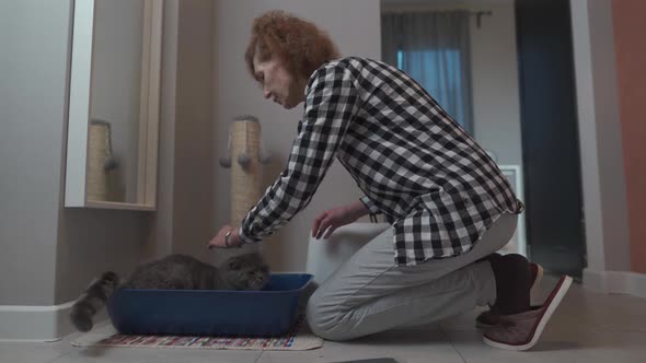 Elderly Pet Owner Prepares Indoor Cat Litter Box with Scottish Straight Cat at Home