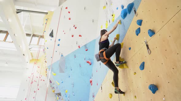 Woman lead climbing up a wall in an indoor climbing center