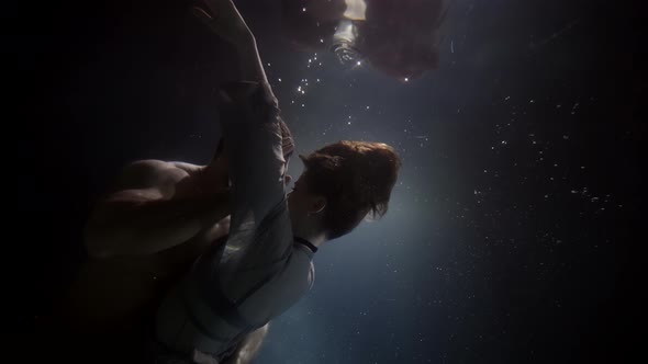 A Man Spins and Dances Beautifully with His Woman Underwater Lovers Deep Inside on a Dark Background