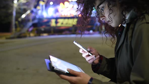 Young beautiful mixed race woman outdoor in the city night using smart phone and tablet