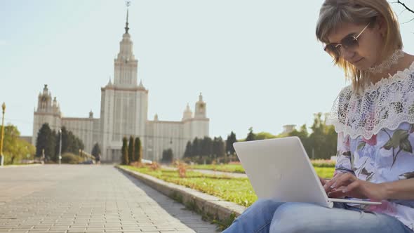 Female Student Working with a Laptop on a Square on the Background of Lomonosov Moscow State