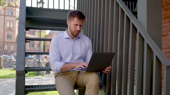 Young Businessman Sitting on Spiral Stairs and Using Laptop Outdoors