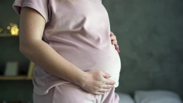 Happy Pregnant Woman Standing on Bedroom Holding and Stroking Her Big Belly at Home Close Up