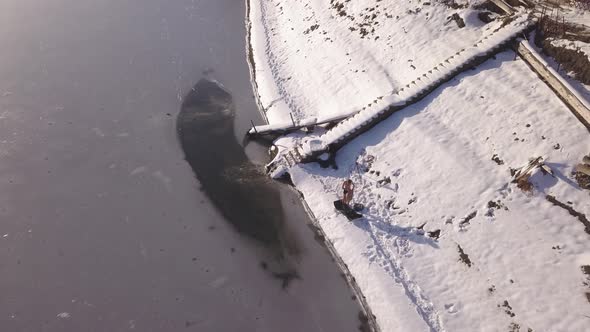 Drone descending near shore of frozen lake with man drying off using towel after ice swimming. Polar
