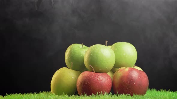 Fresh apples with droplets of water against black background on rotating grass surface.