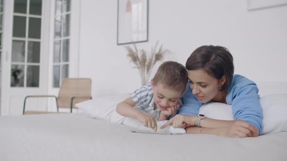 Mother and Son Using Digital Tablet in Bedroom at Home