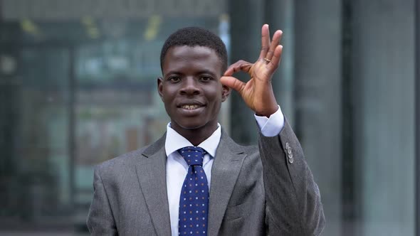 Smiling young African businessman makes OK with his hand - slow motion