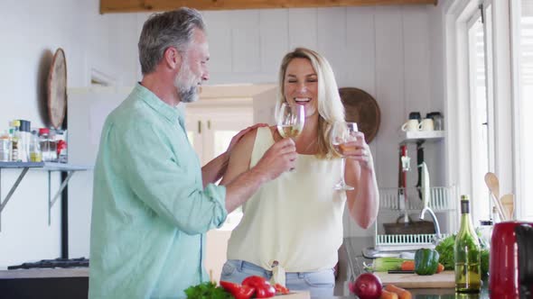 Happy caucasian mature couple cooking together and drinking wine in the kitchen