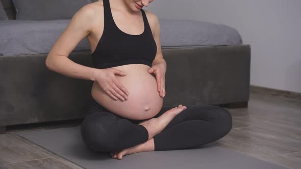 A Calm Pregnant Woman Holds Her Hands on Her Stomach Meditating on the Floor of the House in Sports