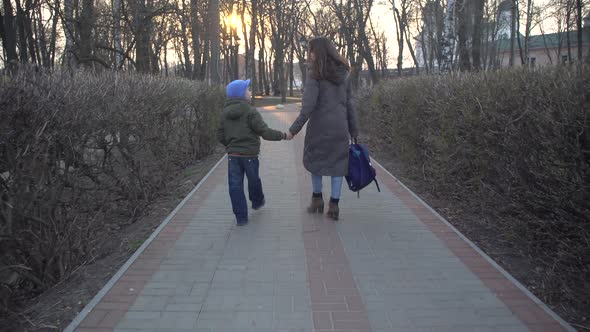 Back View of Young Brunette Caucasian Woman and Little Schoolboy Walking Along the Alley in City